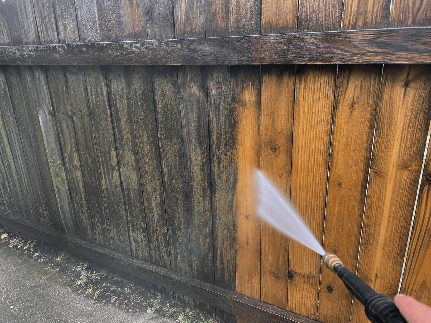 High-pressure water cleaning a weathered wooden fence, revealing the bright, natural wood grain underneath.