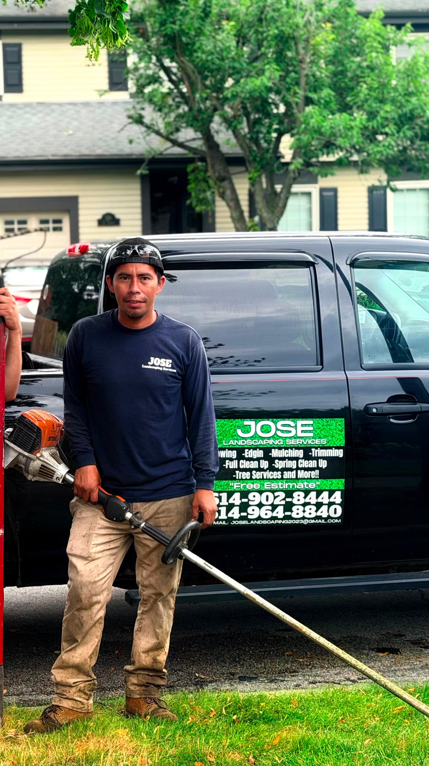 Landscaper holding a string trimmer stands in front of a black Jose Landscaping service truck.